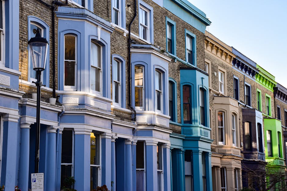 A row of multi-story Victorian terraced houses with detailed architectural features, including large bay windows, decorative cornices, and brick facades painted in pastel shades of blue, beige, and gr